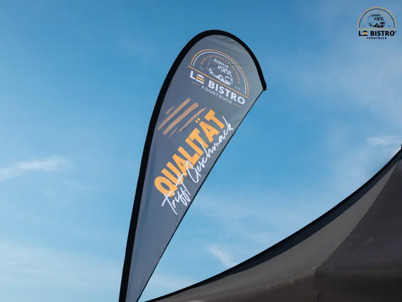 Beachflag von Le Bistro Foodtruck mit dem Schriftzug „Qualität trifft Geschmack.“ vor blauem Himmel