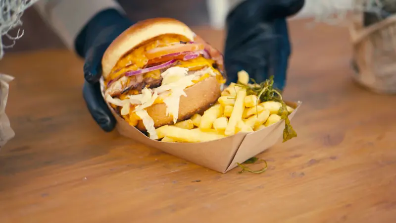 Fertiger Le-Bistro-Burger mit Pommes in der Papierschale auf dem Holztresen