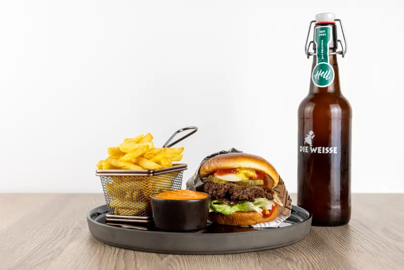 Le-Bistro-Burger mit Pommes im Drahtkorb, Dip und einer Flasche Bier auf dem Holztisch