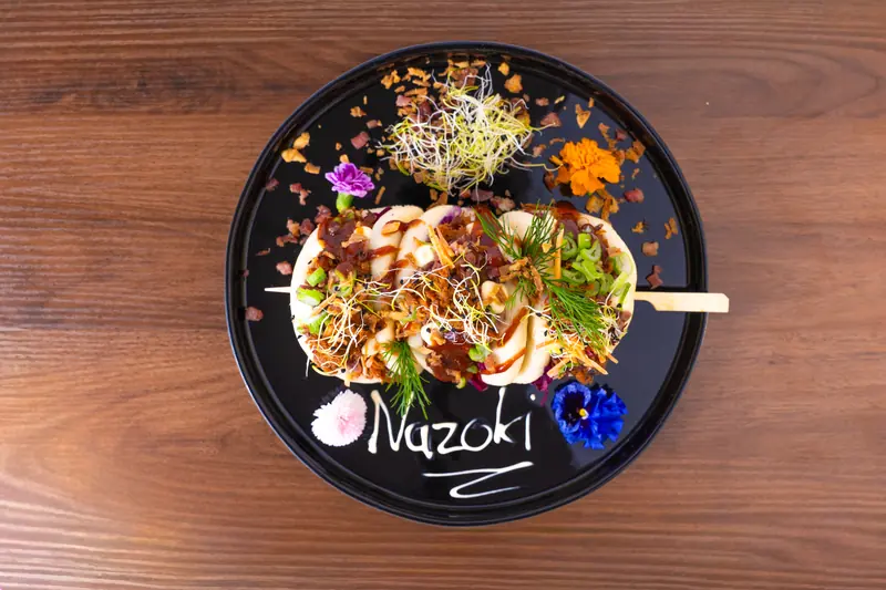 Bio Beef Bao Buns von Nazoki mit essbaren Blüten, von oben, „Nazoki“ auf den Teller geschrieben