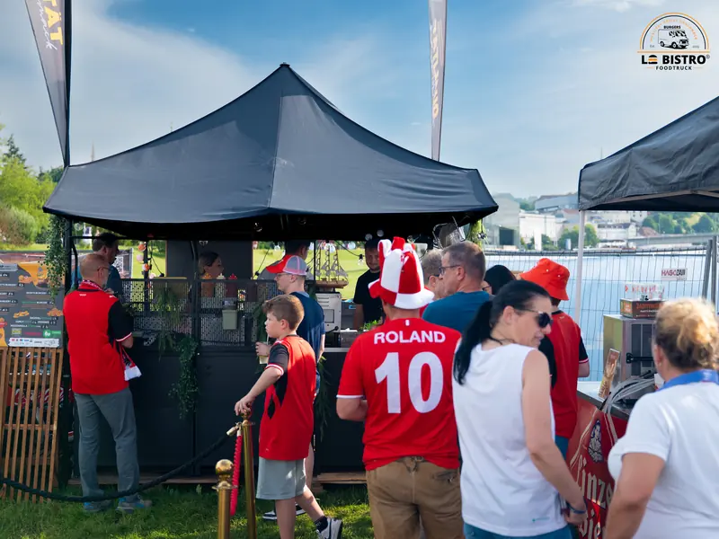 Gäste an einem Stand mit schwarzem Zelt, Public Viewing Sandburg Linz
