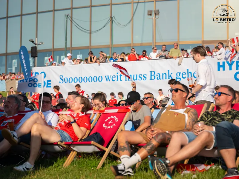 Fans in Liegestühlen vor einem Werbebanner, Public Viewing Sandburg Linz