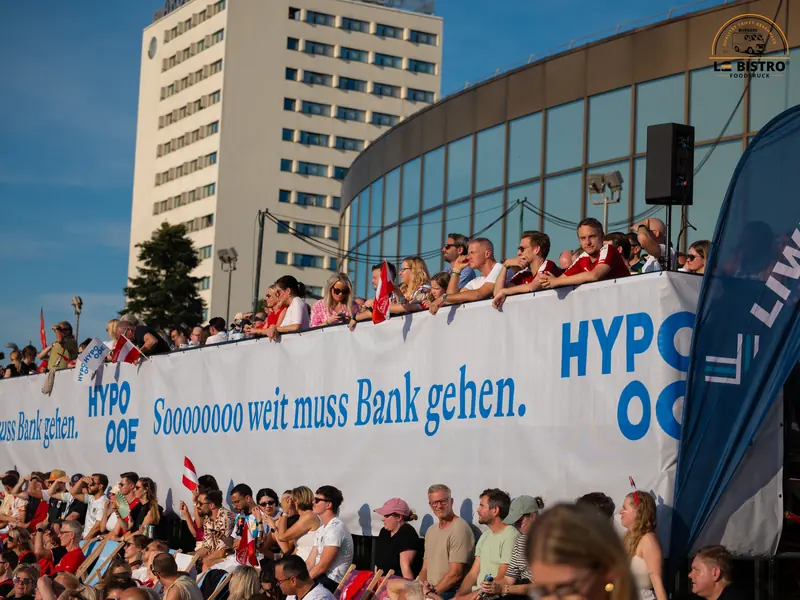 Fans hinter einem Werbebanner, Public Viewing Sandburg Linz