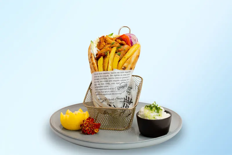 Original Gyros von Tiligo: Pita mit Chicken, Pommes und Tzatziki im Drahtkorb vor hellblauem Hintergrund